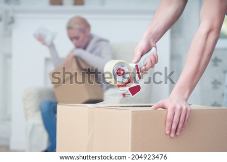 Selected focus on the box which is pasted up by some man. Attractive blonde sitting on the cosy sofa on background