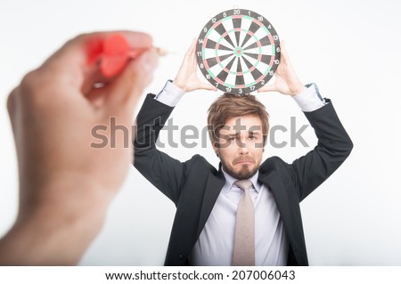 Poor man standing with the dartboard on his head waiting of hitting the target