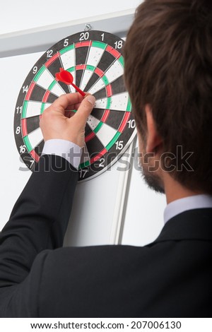 Portrait of dark-haired bearded man standing back to us attaching dart on target