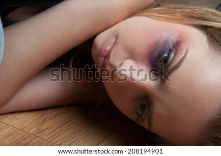 Poor young fair-haired woman with the black eye lying on the floor reassuring herself that everything will be ok