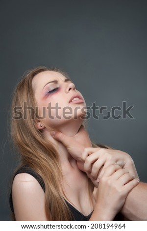 Poor young woman with the black eye standing aside to us suffering from the pain. Her husband wants to strangle her. Isolated on grey background