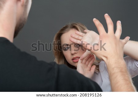 Young man wearing black shirt wanted to cuff poor fair-haired girl shut herself with her hands. Isolated on grey background