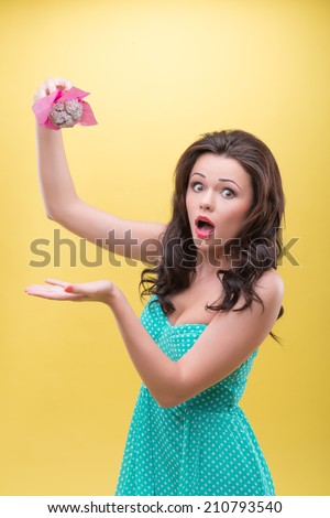 Half-length portrait of sexy dark-haired woman frightened that her doughnut will fall on the floor. Isolated on yellow background