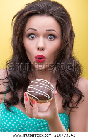 Half-length portrait of very excited dark-haired woman getting to know how many calories her appetizing round doughnut covered with the chocolate icing has. Isolated on yellow background