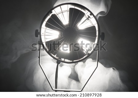 Switched cinema spotlight standing in the dark enveloped in smoke