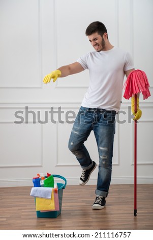 Full-length portrait of very angry dark-haired janitor wearing white shirt blue torn jeans and yellow rubber gloves standing with the red mop wanted to throw pail with cleansers