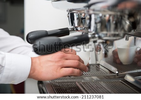 Hands of professional barista putting the cup of on the grating of coffee machine
