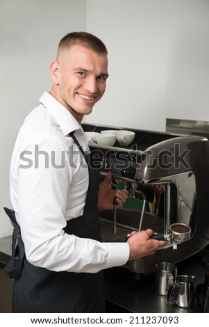 Half-length portrait of handsome young smiling barista making coffee for us using coffee machine