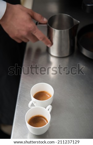 Two cups of americano standing on the bar counter near the metal jar for milk