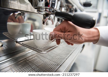 Hands of professional barista holding two white cups on the grating of coffee machine
