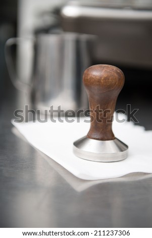 Selected focus on the little pounder with wooden handle for coffee lying on the napkin. Metal glass on background