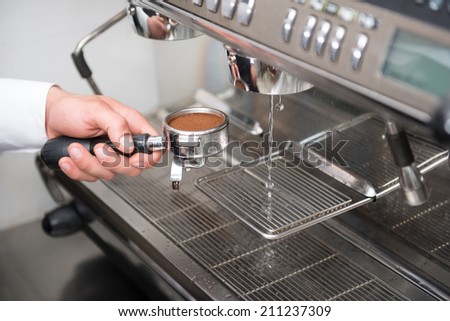 Hands of professional barista holding the form with pressed coffee near running water in the coffee machine