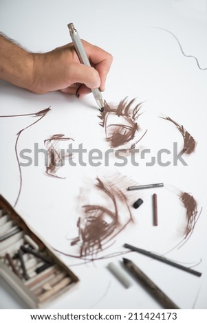 Painter drawing the picture with the lead pencils on the big white sheet of paper