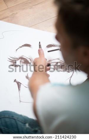 Painter drawing the picture with the lead pencil on the big white sheet of paper lying on the floor