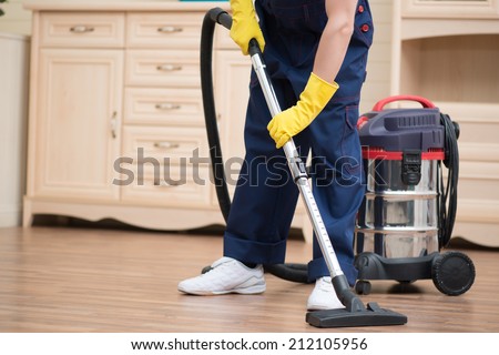 Selective focus on janitor wearing blue overalls vacuuming the floor in the office. Commode on background
