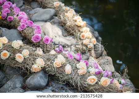 Very nice strips made of violet and peach-colored roses hanging down from the stones into the water