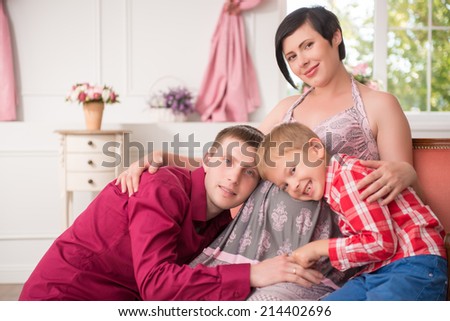 Selective focus on the lovely happy pregnant woman sitting in the chair and smiling man and his little son leaning to the belly of their mom. Their living room on background