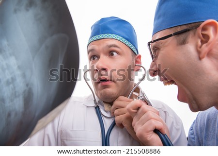 Half-length portrait of two excited doctors wearing blue caps one of them keeping a stethoscope and another says something in it looking at the radiograph astonished. Isolated on white background
