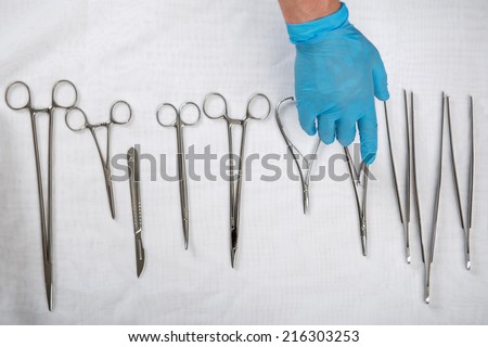 Doctor wearing blue disposable gloves choosing the necessary one from the medical instruments lying on the white material