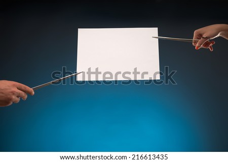 White sheet of paper for copy place is held by someone with the help of scissors. Isolated on blue background