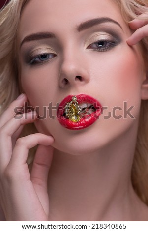 Half-length portrait of beautiful sexy blonde with red tempting lips and perfect skin holding wonderful fingering with topaz in her mouth touching her face isolated on dark background