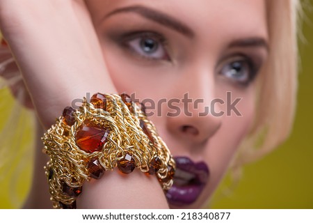 Half-length portrait of beautiful sexy blonde with violet tempting lips and perfect skin showing us her precious gold bracelet isolated on yellow background. Close up
