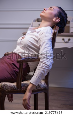 beautiful dark-haired young sapless woman wearing white blouse and vinous skirt sleeping in the chair. Her office on background