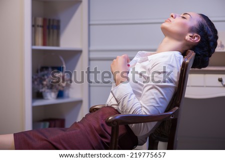 woman wearing white blouse and vinous skirt sleeping in the chair. Her office on background