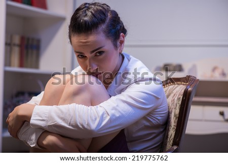 woman wearing white blouse sitting in the chair flexing her legs and thinking how to solve her problems. Her office on background