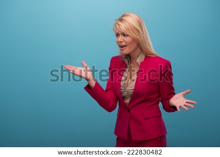 Half-length portrait of very beautiful fair-haired excited TV presenter wearing great red jacket and cream-colored shirt proving something. Isolated on blue background