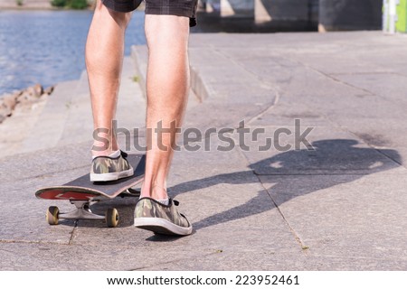 Half-length portrait of the man wearing shorts and trainers riding a skateboard on the quay