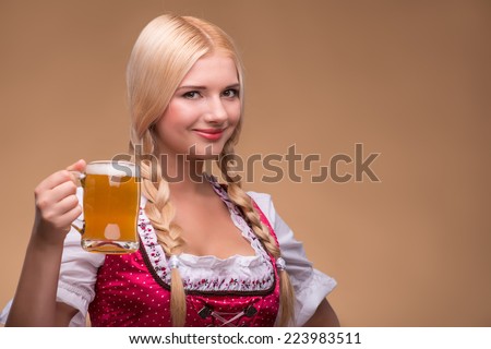 Young sexy smiling blonde wearing pink dirndl with white blouse holding beer mug showing us how she likes it. Isolated on dark background