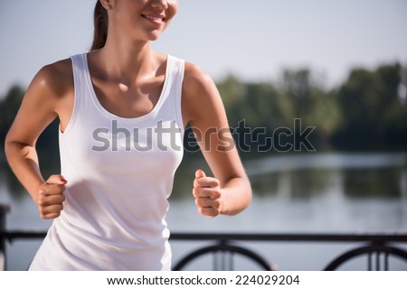 Selective focus on the young sexy woman wearing white T-shirt running near the river