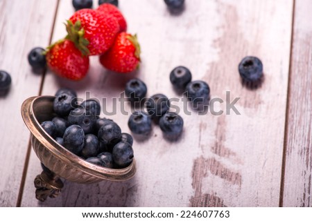 Selective focus on the red tempting strawberries lying on the table near the heap of delicious blackberries on background. Top view