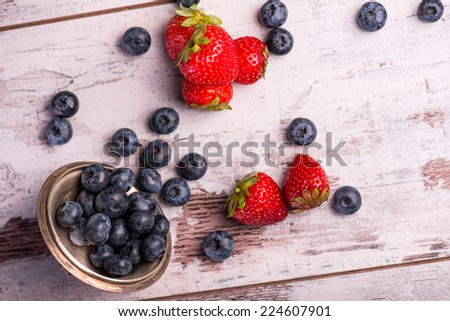Still life with the copper top and little blackberries in it scattering on the wooden table amid the tempting red strawberries. Top view