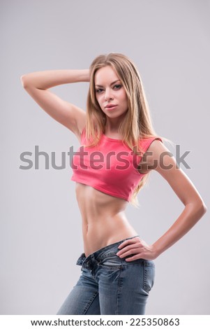 Half-length portrait of sexy beautiful blonde with great figure wearing pink vest and jeans standing aside looking at us seductively. Isolated on white background