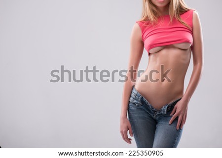 Half-length portrait of sexy beautiful blonde with great figure wearing pink vest and jeans showing us her tempting belly. Isolated on white background