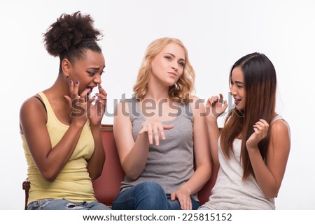 Half-length portrait of three pretty smiling girls wearing jeans and T-shirts sitting on the sofa discussing the engagement of one of them. Isolated on white background