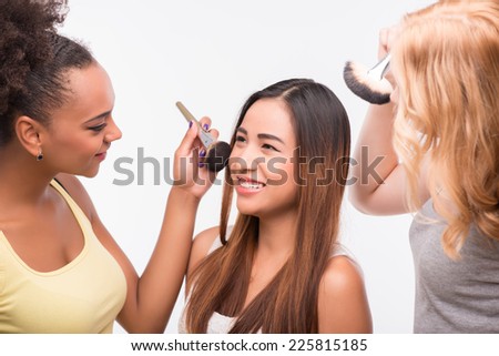 Half-length portrait of two beautiful girls doing make up their best friend sitting and smiling. Isolated on white background