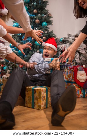Half-length portrait of very greedy but funny guy lying on the floor wearing red cap of Santa Claus holding presents do not giving them to someone