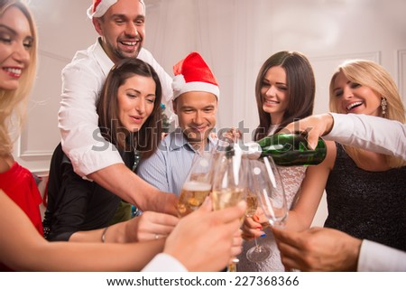 Half-length portrait of the company of happy young friends standing in a circle pouring the champagne greeting each other with the New Year