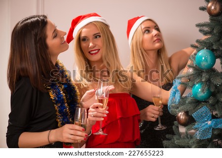 Half-length portrait of three happy smiling women standing near the Christmas tree decorated it and drinking champagne