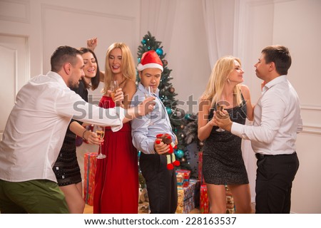 Full-length portrait of the company of happy friends wearing great costumes dancing near the Christmas tree celebrating New Year drinking champagne