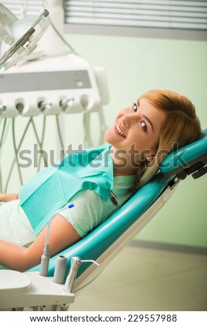 Half-length portrait of nice smiling blonde sitting in the dentist chair looking at us