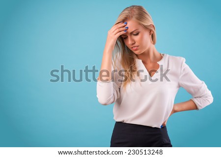 Half-length portrait of beautiful tired blonde wearing white classic blouse and black skirt standing touching her head. Isolated on blue background