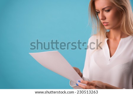Half-length portrait of beautiful business lady wearing white classic blouse standing aside looking at the white sheet of paper for copy place. Isolated on blue background