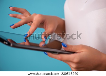 Half-length portrait of the business lady wearing white classic blouse standing aside looking for something in her tablet. Isolated on blue background