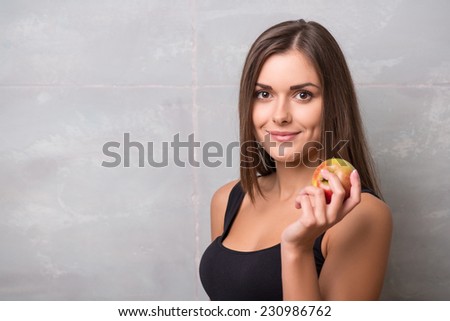 Half-length portrait of sexy smiling dark -haired young woman wearing black vest holding very delicious ripe apple wanted to share with us