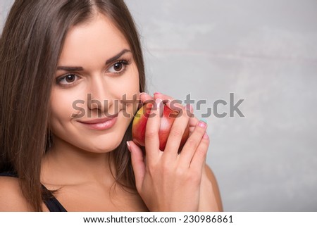 Half-length portrait of lovely smiling dark -haired young woman wearing black vest hugging very delicious ripe apple