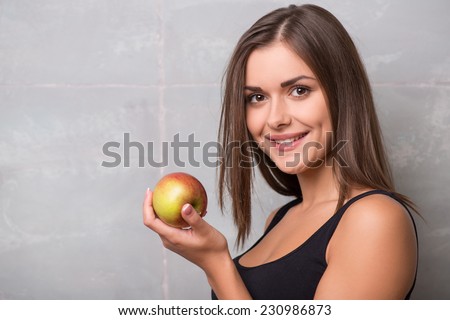 Half-length portrait of sexy smiling dark -haired young woman wearing black vest holding very delicious ripe apple wanted to share with us